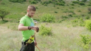 Genç bir adam bir hedefe ok atar, doğada, ve hedefi vurur, ok hedefi uçmak için delip geçer, yay telini sıkıca çeker. Prores 422