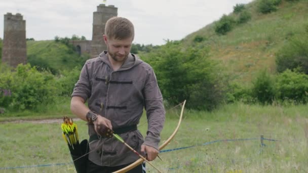 A young guy shoots a bow at a target, in nature, and hits the target, the arrow pierces the target for flight, pulls the bowstring tightly for a shot. Prores 422 — Stock Video