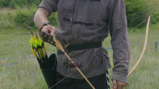 Een jongeman schiet een boog op een doel, in de natuur, en raakt het doel, de pijl doorboort het doel voor de vlucht, trekt de boogpees strak voor een schot. Prores 422 — Stockvideo