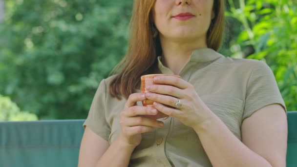 A young girl in the summer drinks hot tea, sitting on a swing, in her yard, tea helps in the heat best of all, Prores422 — Stock Video