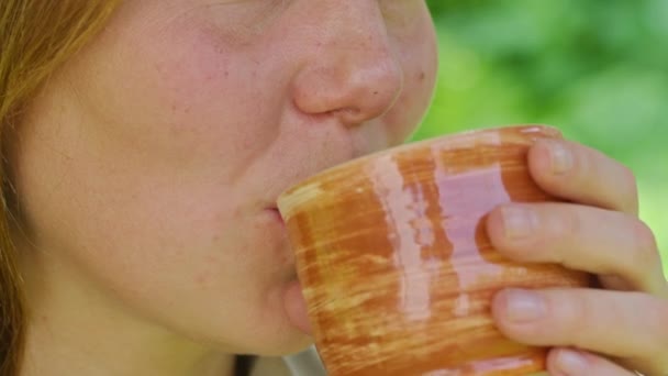 A young girl in the summer drinks hot tea, sitting on a swing, in her yard, tea helps in the heat best of all, Prores422 — Stock Video