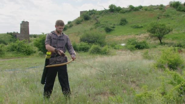 Молодой парень стреляет луком в мишень, в природе, и попадает в мишень, стрела пробивает мишень для полета, крепко дергает луковую нить для выстрела. Прорес 422 — стоковое видео