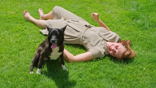 Una joven en el verano juega en el césped con un perro, lo rasca mientras lo lame y disfruta. Prores422. — Vídeos de Stock