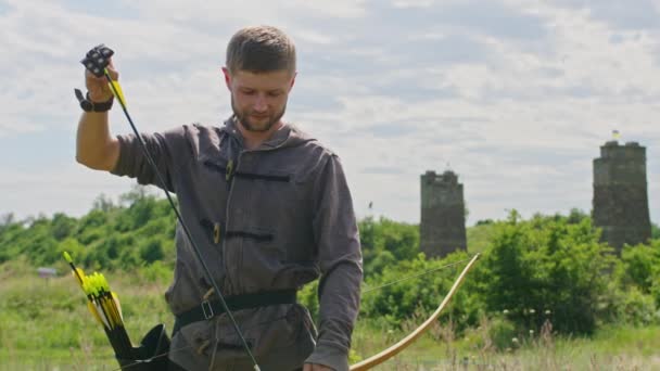 Een jongeman schiet een boog op een doel, in de natuur, en raakt het doel, de pijl doorboort het doel voor de vlucht, trekt de boogpees strak voor een schot. Prores 422 — Stockvideo