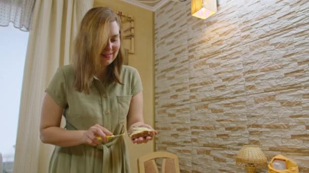 Commerciële beelden, een jong meisje snijdt brood met een mes, spreidt een boterham met boter en giet honing, danst en eet een sandwich, glimlacht naar de camera. Prores422 — Stockvideo