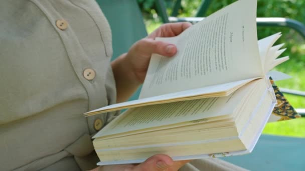 Riprese commerciali, una giovane ragazza in estate in giardino legge un libro, seduta su un'altalena. — Video Stock