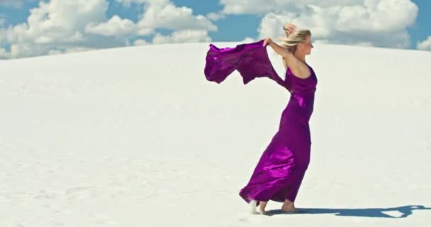 电影中一个女人在沙丘上行走的缓慢动作。赤脚女旅行者穿着连衣裙，在风中摇曳着，在沙质沙漠起伏的表面上，身后是一片云彩。4K场景 — 图库视频影像