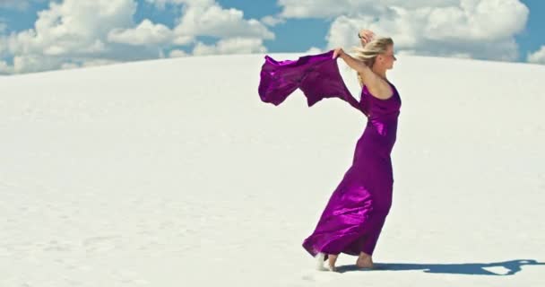 Cinemática cámara lenta de una mujer caminando sobre una duna de arena. Viajante descalza en un vestido balanceándose en el viento sobre la ondulante superficie del desierto de arena con una nube en el fondo. 4K Escénico — Vídeo de stock