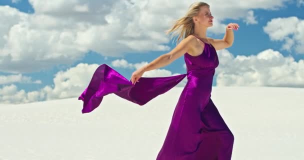 Kum tepeciğinde yürüyen bir kadının sinematik yavaş çekimi. Çıplak ayaklı kadın gezgin rüzgarda sallanan bir elbiseyle kumlu çölün dalgalı yüzeyinde arka planda bir bulutla. 4K Manzarası — Stok video