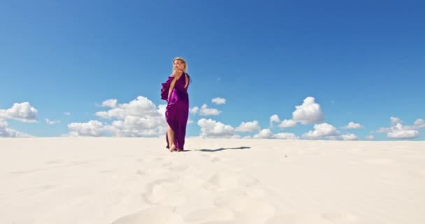 Cinemática cámara lenta de una mujer caminando sobre una duna de arena. Viajante descalza en un vestido balanceándose en el viento sobre la ondulante superficie del desierto de arena con una nube en el fondo. 4K Escénico — Vídeo de stock