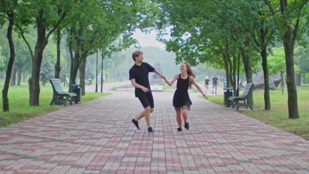 A young couple, a guy and a girl are running along the alley in the park, hugging, fooling around, showing feelings to each other. — Stock Video