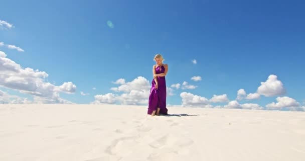Cinemática cámara lenta de una mujer caminando sobre una duna de arena. Viajante descalza en un vestido balanceándose en el viento sobre la ondulante superficie del desierto de arena con una nube en el fondo. 4K Escénico — Vídeo de stock