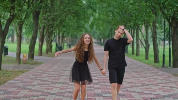 Mladý pár, muž a dívka běží uličkou v parku, objímají se, pohrávají si, ukazují si navzájem city. — Stock video