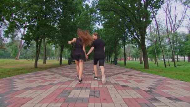 Een jong stel, een jongen en een meisje rennen door het steegje in het park, knuffelen, rotzooien, tonen gevoelens aan elkaar. — Stockvideo