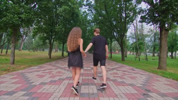 Egy fiatal pár, egy fiú és egy lány rohangálnak a sikátorban a parkban, ölelkeznek, hülyéskednek, érzelmeket mutatnak egymásnak.. — Stock videók