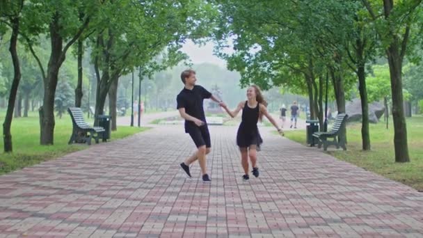 Een jong stel, een jongen en een meisje rennen door het steegje in het park, knuffelen, rotzooien, tonen gevoelens aan elkaar. — Stockvideo