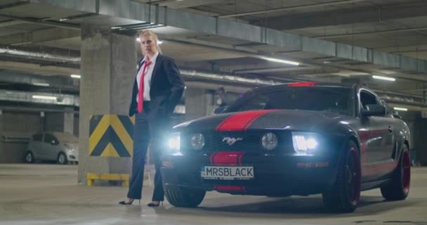 Krásná blondýna v černém obleku, bílá košile a červená kravata vystoupí ze svého černého auta na podzemním parkovišti, filmový záběr, zpomalený film. — Stock video