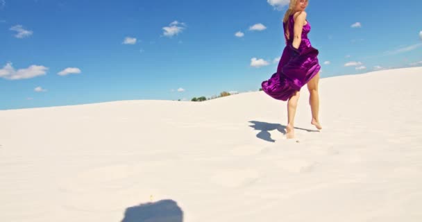 Cinemática cámara lenta de una mujer caminando sobre una duna de arena. Viajante descalza en un vestido balanceándose en el viento sobre la ondulante superficie del desierto de arena con una nube en el fondo. 4K Escénico — Vídeo de stock