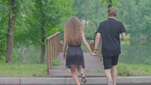 Een jong stel, een jongen en een meisje die langs de dijk in het park rennen, knuffelen, rotzooien, gevoelens voor elkaar tonen. — Stockvideo