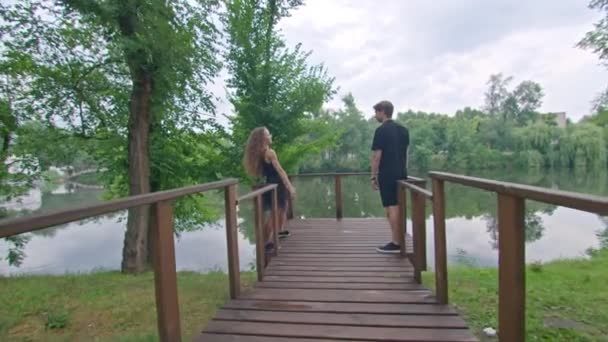 Um jovem casal, um cara e uma menina correndo ao longo do dique no parque, abraçando, brincando, mostrando sentimentos um pelo outro. — Vídeo de Stock