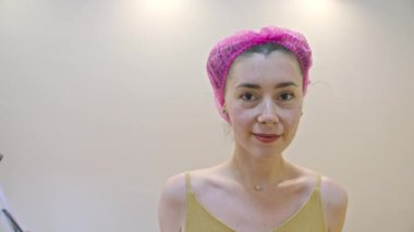 Ameliyattan sonra güzellik muayenehanesinde dikilirken kameraya bakan kendinden emin, genç Avrupalı bir kadın..