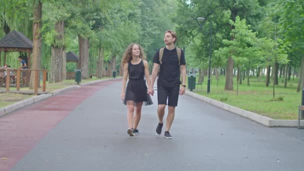 Un jeune couple, un mec et une fille courant le long du remblai dans le parc, s'embrassant, s'amusant, montrant des sentiments l'un pour l'autre. — Video