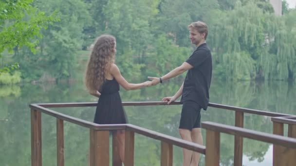 Un jeune couple, un mec et une fille courant le long du remblai dans le parc, s'embrassant, s'amusant, montrant des sentiments l'un pour l'autre. — Video