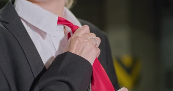 Красивая блондинка в черном костюме, белая рубашка выпрямляет красный галстук, оглядывается на подземную парковку, кинематографический снимок, замедленное движение. — стоковое видео