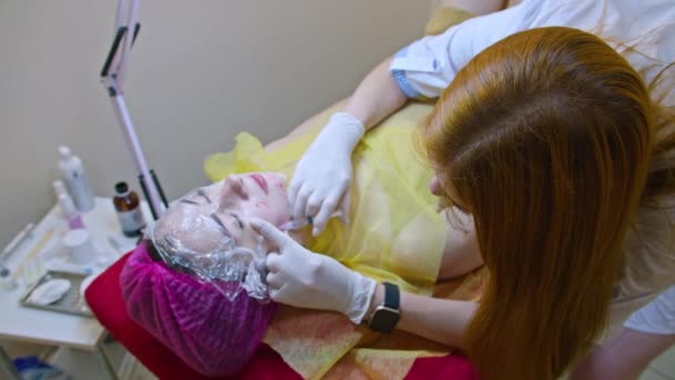 Conceito de beleza e injeção. Cosmetologia na clínica. Um esteticista experiente usando luvas brancas injeta uma injeção subcutânea com os ingredientes ativos necessários em um rosto de mulher para — Vídeo de Stock