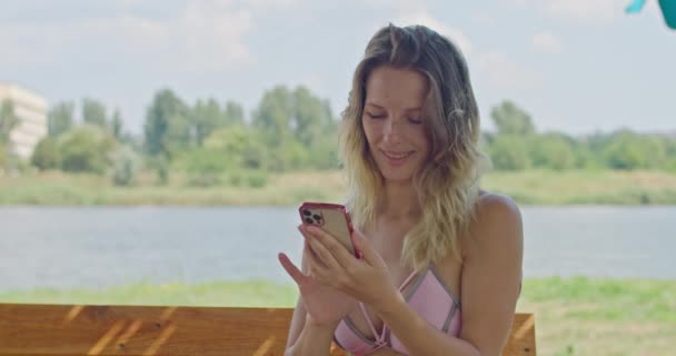 Blonde girl uses the phone, runs her finger across the screen — Stock Video