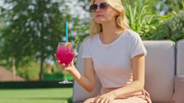 A beautiful young woman in a white t-shirt is enjoying a wonderful cocktail in hot summer in a cool and beautiful place. — Stock Video