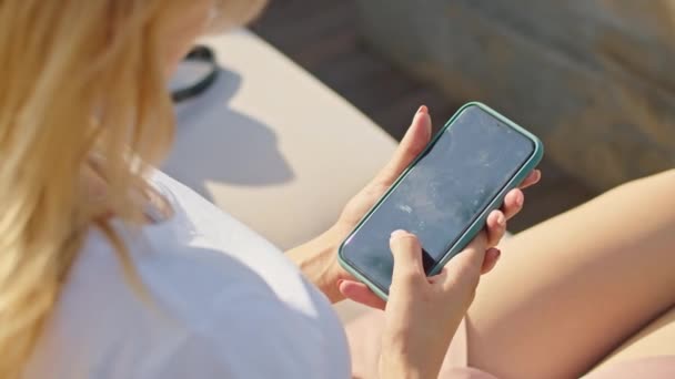 Joven mujer disfruta hablando por teléfono, mensajes de texto con alguien, en un lugar maravilloso, sentado en una camiseta blanca — Vídeo de stock