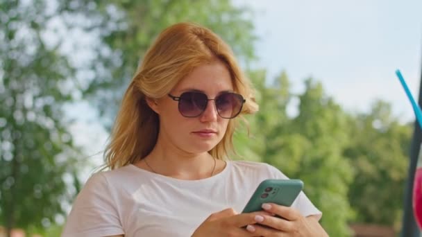 Молодая женщина наслаждается разговорами по телефону, смс с кем-то, в прекрасном месте, сидя в белой футболке — стоковое видео