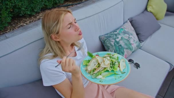 Mladá žena si vychutnává lahodný salát z kuřete, rajčat a krutonů, jí ho vidličkou, na krásném chladném místě v horkém létě. — Stock video