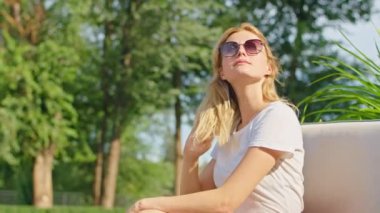 Güzel bir yerde güneşli bir günün tadını çıkarırken beyaz tişörtlü güzel bir kadın birine el sallıyor..