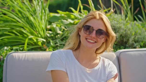 Красивая молодая женщина наслаждается летним днем, улыбаясь, поворачивая голову, сидя в белой футболке в красивом прохладном месте. — стоковое видео