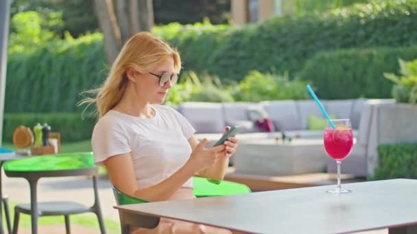 Молодая женщина наслаждается разговорами по телефону, смс с кем-то, в прекрасном месте, сидя в белой футболке — стоковое видео