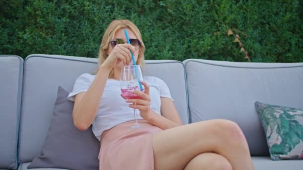 Красивая молодая женщина в белой футболке наслаждается прекрасным коктейлем в жаркое лето в прохладном и красивом месте. — стоковое видео