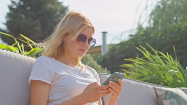 Junge Frau genießt es, mit jemandem zu telefonieren, SMS zu schreiben, an einem wunderbaren Ort, in einem weißen T-Shirt sitzend — Stockvideo