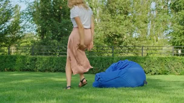 Una giovane donna sta godendo di un posto meraviglioso fresco in estate calda, divertirsi, cadere su un pouf, saltare, ridere, correre sull'erba verde. — Video Stock