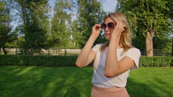 Jeune femme jouit dans un bel endroit, met des lunettes de soleil, se réjouit, regarde la caméra — Video