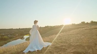 Gün batımında mutlu genç bir gelin, bir dağ tepesinde duruyor, nehrin hoş manzarasının tadını çıkarıyor..