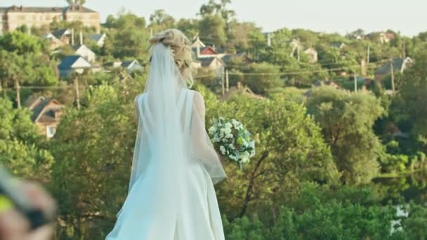 Šťastná mladá žena nevěsta se svatební kytice stojí na pozadí řeky, — Stock video