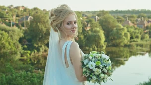 Jeune mariée heureuse avec un bouquet de mariage se tient sur le fond de la rivière, — Video