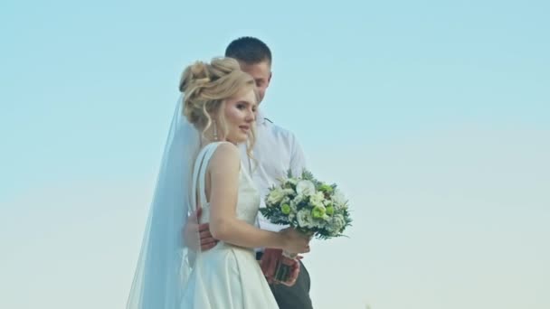 Das Hochzeitspaar kommuniziert auf dem Hintergrund des Himmels, die Braut mit einem Blumenstrauß. auf einem Felsen stehend. — Stockvideo