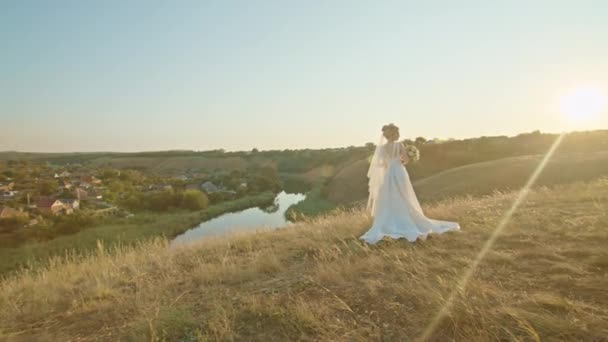 Noiva jovem feliz ao pôr do sol, de pé em uma colina de montanha, desfrutando de uma vista agradável do rio. — Vídeo de Stock
