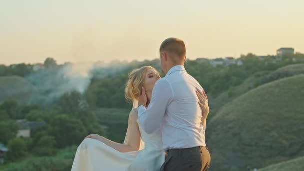 Düğün çifti gün batımında nehrin kenarındaki bir kayanın üstünde eğleniyor. — Stok video