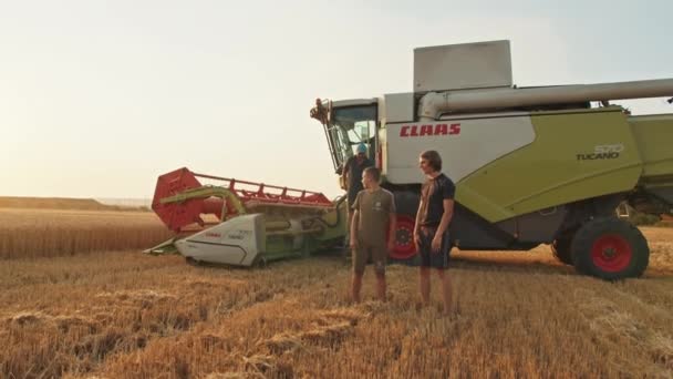 Krivoy Rog, Ukraina - 07.18.2021 bonden och hans söner står mot bakgrund av en skördetröska i fält, jordbruksindustri, skörd, sommar. solnedgång. — Stockvideo