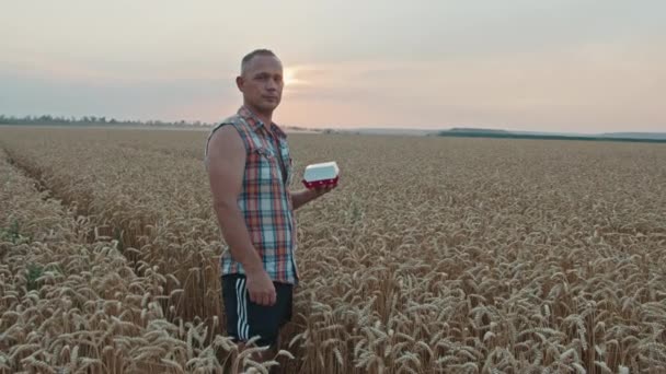 KriwojRog, Ukraine - 18.07.2021 Ukrainischer Bauer steht mit McDonalds-Burger in einem Weizenfeld — Stockvideo