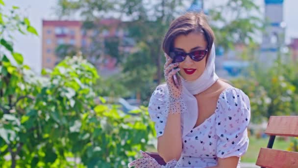 Wanita muda dengan gaun putih yang bahagia berbicara lewat telepon di taman, musim panas. pinup — Stok Video